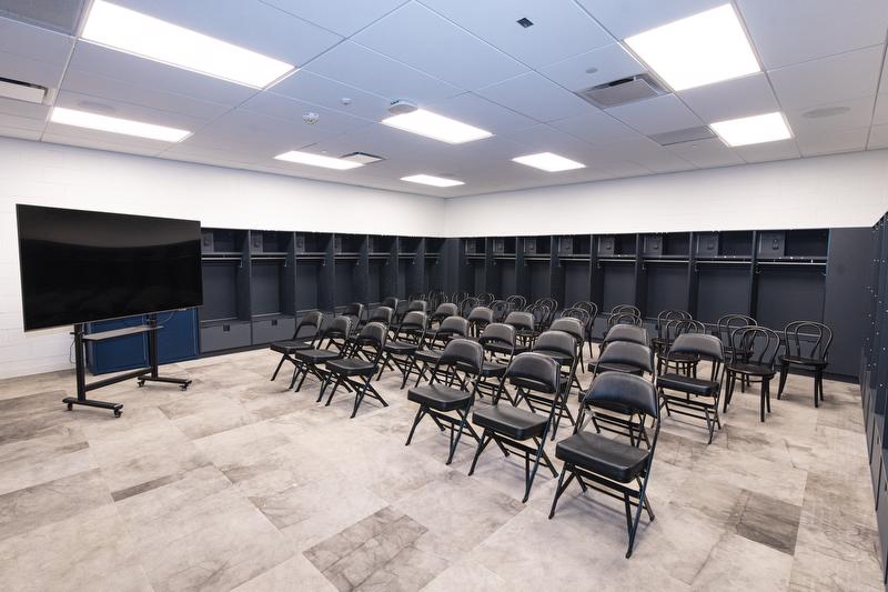 A view of visiting team locker room setup with chairs and TV for presenting.